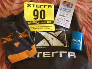 Race T-shirt, race bib with number, race brochure, and X-terra swag bag with Body Glide container arranged together.