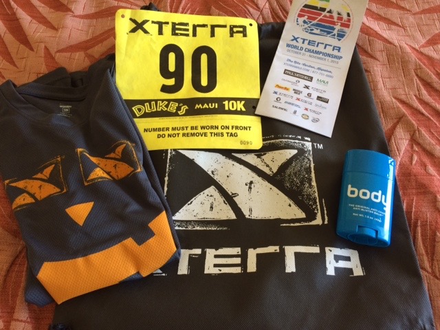 Race T-shirt, race bib with number, race brochure, and X-terra swag bag with Body Glide container arranged together. 