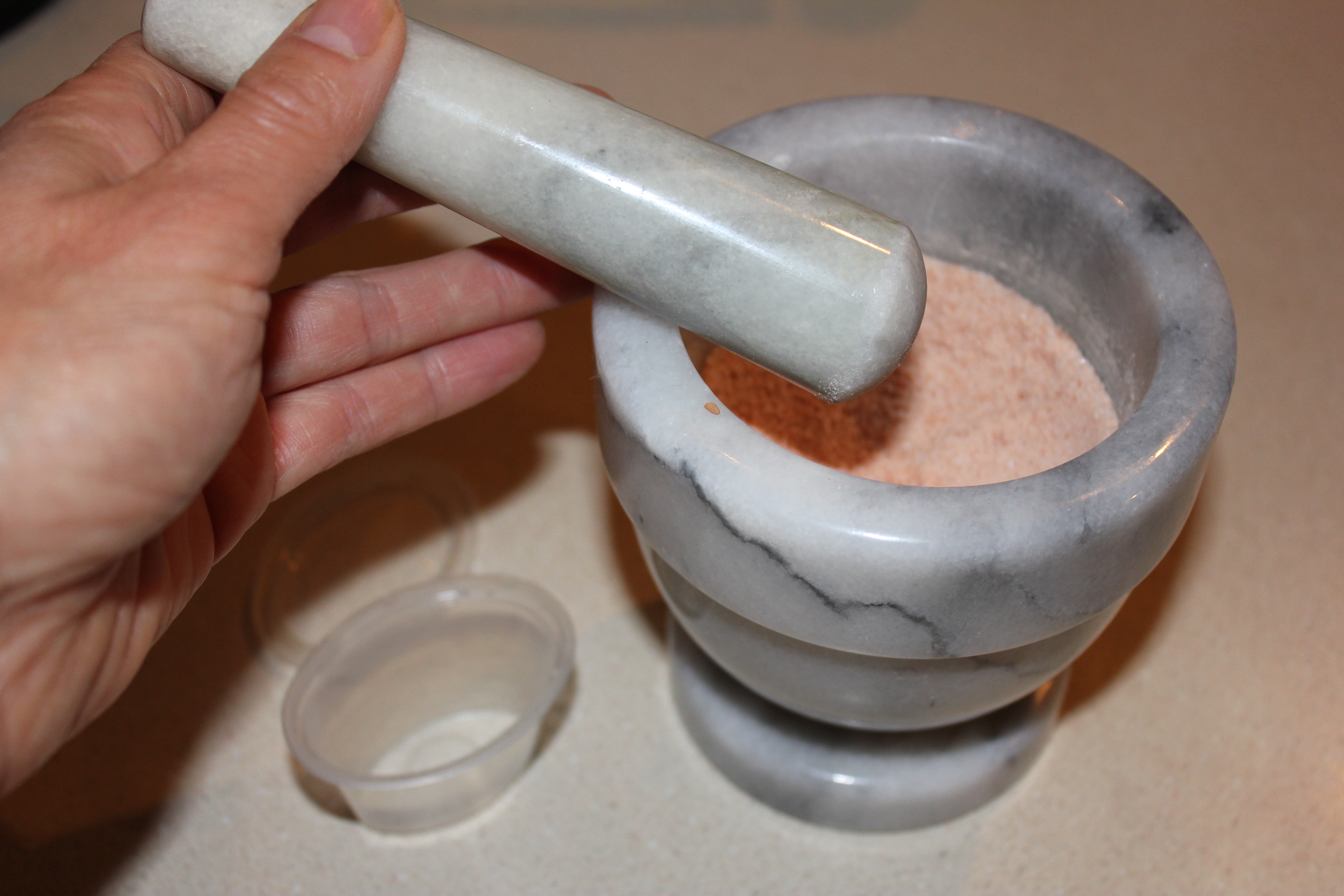 Hand holds pestle, pink salt ground sits in the matching pestle, both in grey and white granite.