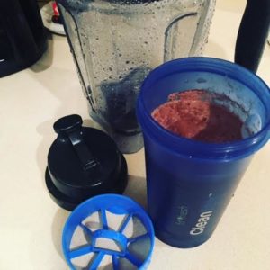 Vitamix pitcher, blue Clean Tek container with strainer insert and lid off to the left side.