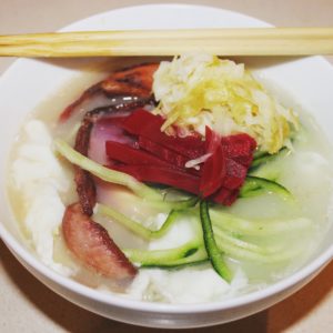 White bowl with noodles, vegetable, beets, bacon, and sauerkraut, with a pair of chopsticks across the top. Photo by Imei Hsu.