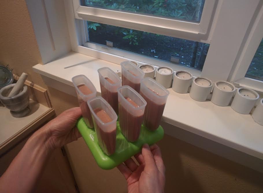 Six plastic ice pop molds with liquid filling in each on a holding tray, next to an open window. 