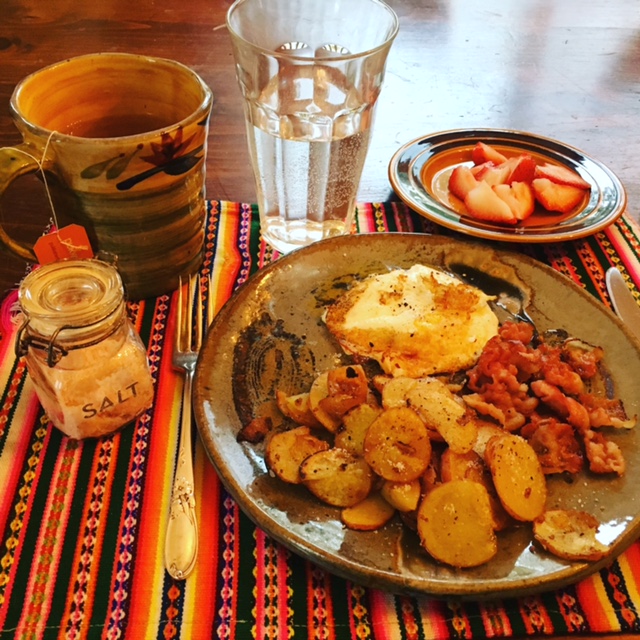 Plate of breakfast foods, fruit, coffee, and salt container sitting on a placemat on a wood table
