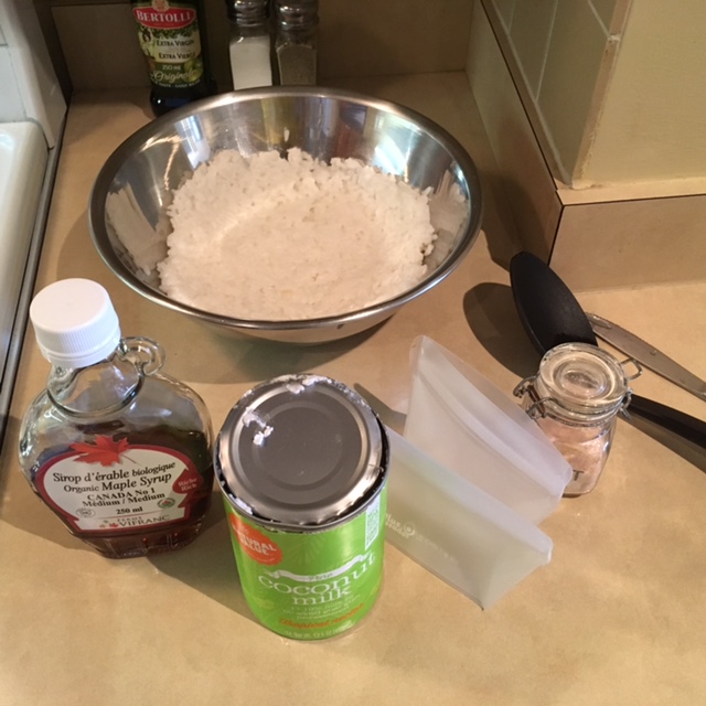 Bowl of rice, can of coconut milk, silicone pouches, container of salt, and bottle of maple syrup, sitting on a kitchen counter