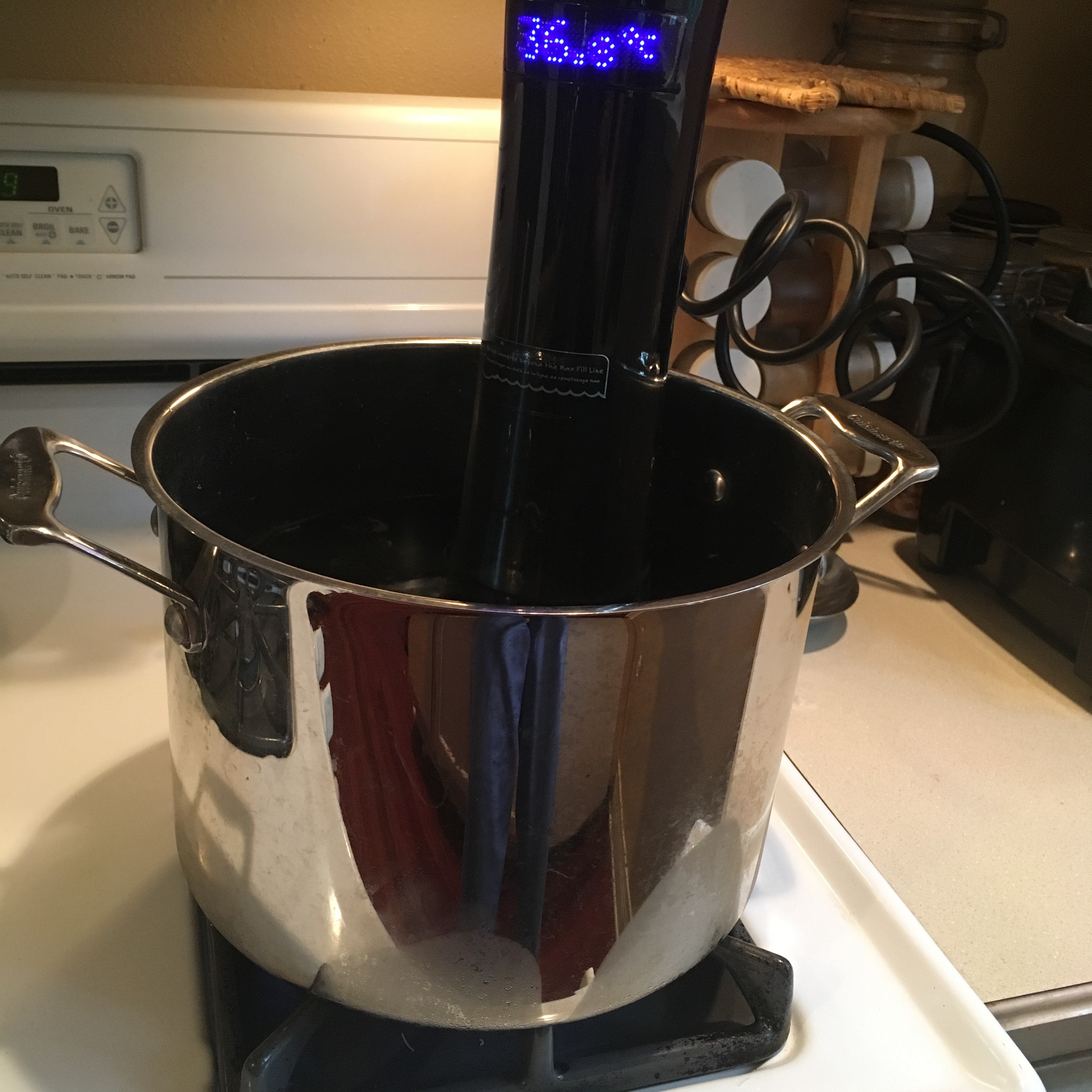 A sous vide circulator, clipped in place to a large pot of water on a stove top, stove is not on. A cord for the circulator is plugged in the wall. Photo by Imei Hsu.