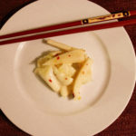 white plate, red chopsticks, seven slender pieces of white daikon root with red pepper flakes in the center of a white plate