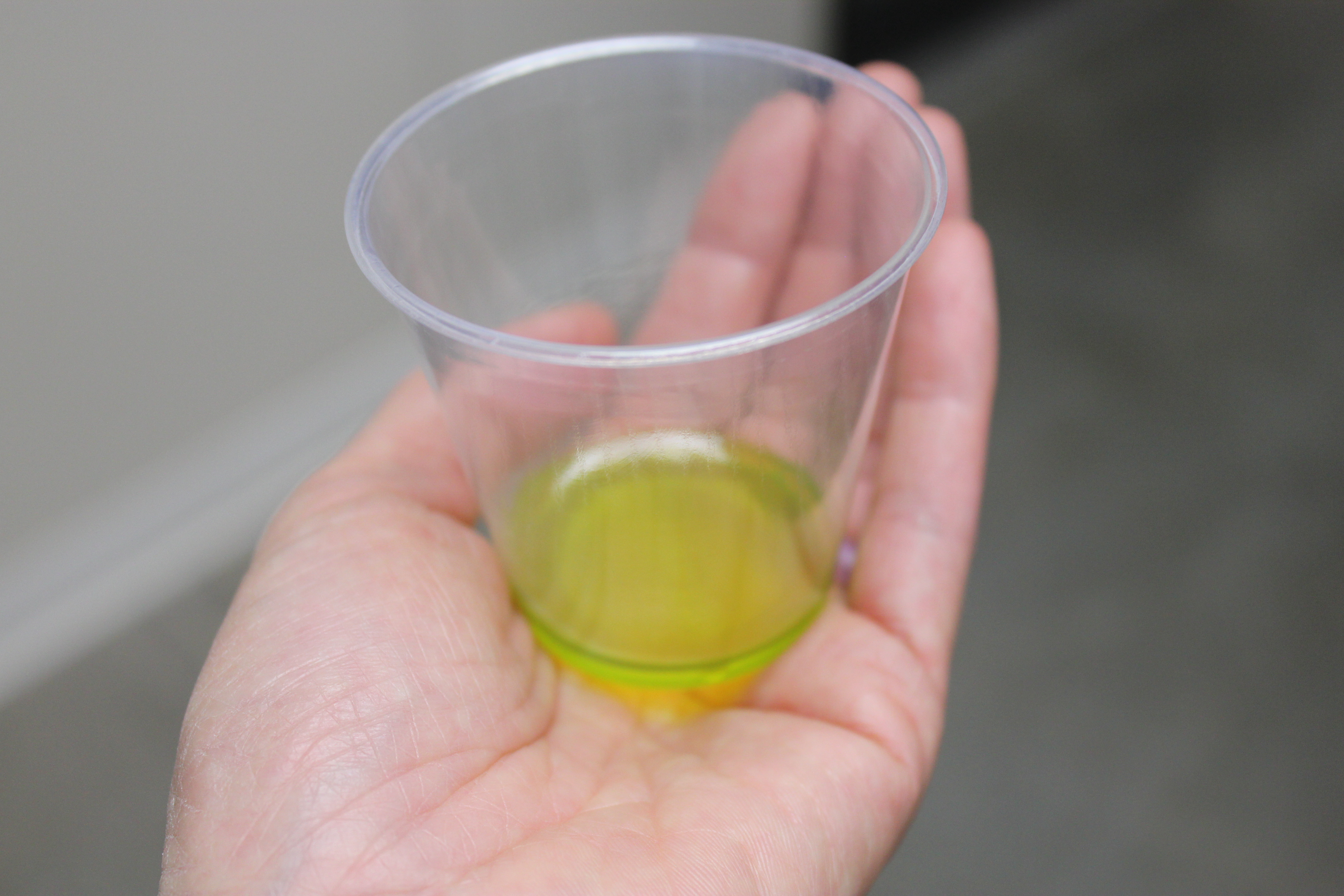 plastic cup with less than a tablespoon of olive oil, held in palm of hand.